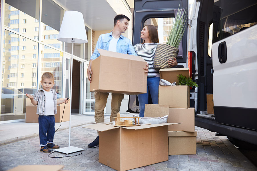 Young family loading boxes and household items into a van outside their new home