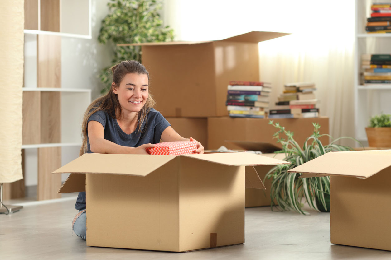 Young woman unpacking belongings from cardboard boxes in her new home