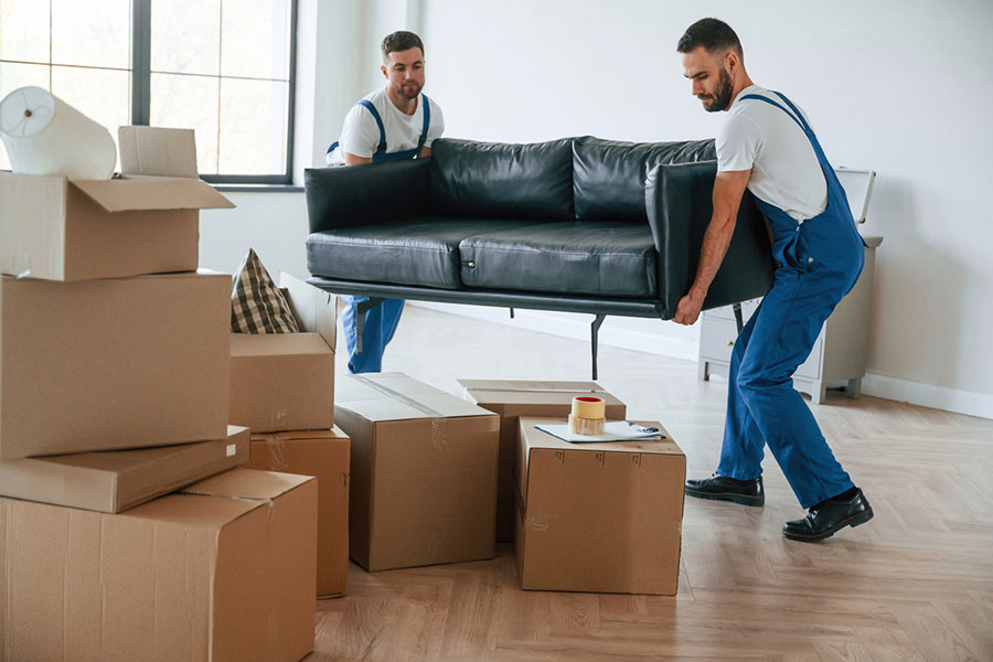 Two removal workers carrying a sofa surrounded by moving boxes